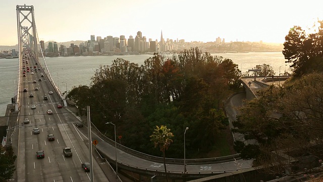 汽车和公共汽车在海湾大桥上行驶，夕阳在大桥后面。视频素材