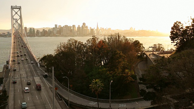 汽车和公共汽车在海湾大桥上行驶，夕阳在大桥后面。视频素材