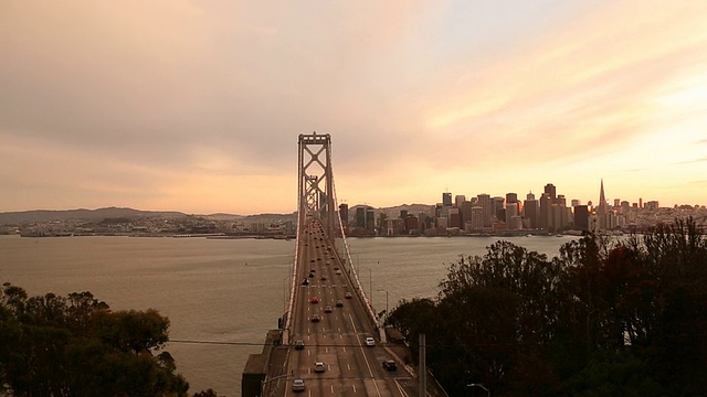 汽车和公共汽车在海湾大桥上行驶，夕阳在大桥后面。视频素材