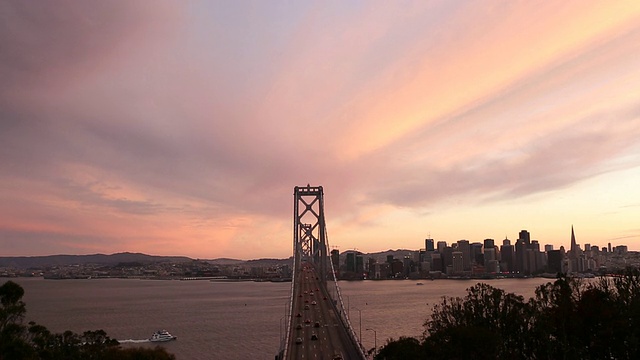 汽车和公共汽车在海湾大桥上行驶，夕阳在大桥后面。视频素材