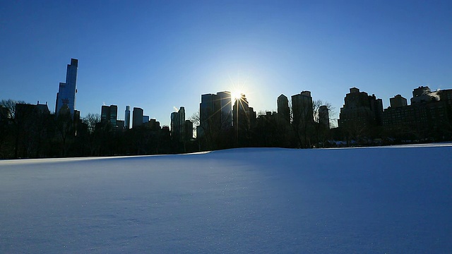 TL相机捕捉到了日落时分在冰雪覆盖的绵羊草地和曼哈顿摩天大楼上方的太阳。视频素材