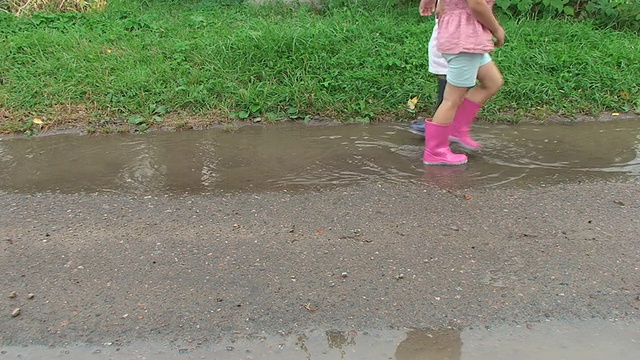 孩子们穿着五颜六色的雨靴踏着泥泞的水坑。视频素材