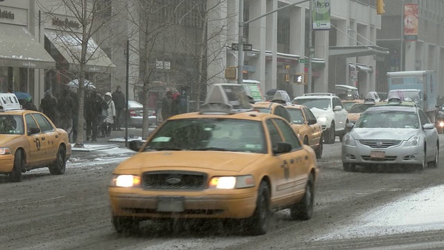 在一个大雪纷飞的冬日里，纽约街道上的车辆在移动。一名骑着助力车的送货员正在穿越。视频素材