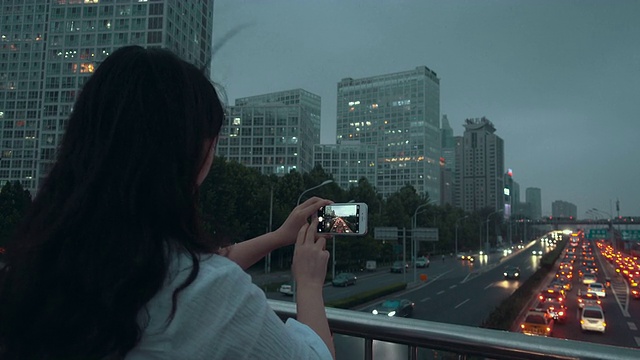 一个女人用手机拍摄城市的夜晚视频素材