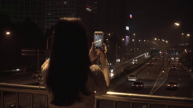 年轻女子用智能手机在城市的夜晚拍照视频素材