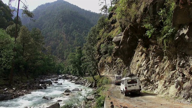 两辆4x4陆地巡洋舰式车辆沿着河流行驶在崎岖的土路在山区。视频素材