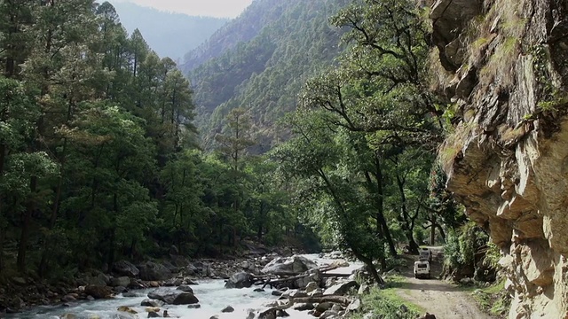 两辆4x4陆地巡洋舰式车辆在崎岖的山路上沿着河流行驶。视频素材