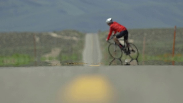 一个男人骑着自行车在一个风景优美的沙漠道路上。——慢动作视频素材