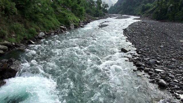 近距离拍摄奔流的河流沿着山谷底部在山区。视频素材