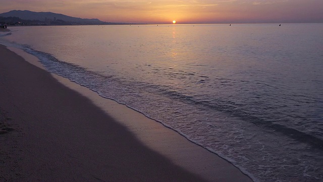 4K:夏季结束时巴达洛纳(巴塞罗那)海滩的日出。我们可以看到平静的地中海在对称的广角拍摄太阳和地平线在顶部三分之一视频素材