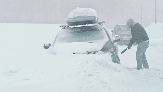 在暴风雪中，一名男子正在把他的车从雪中挖出来视频素材