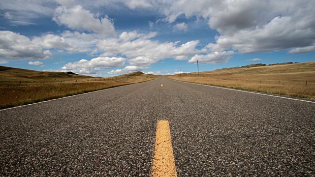 低广角视野的空铺砌道路与蓬松的云和蓝天与阴影滚动横跨景观。视频素材