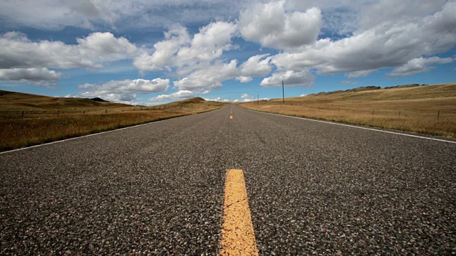 低广角视野的空铺砌道路与蓬松的云和蓝天与阴影滚动横跨景观。视频素材