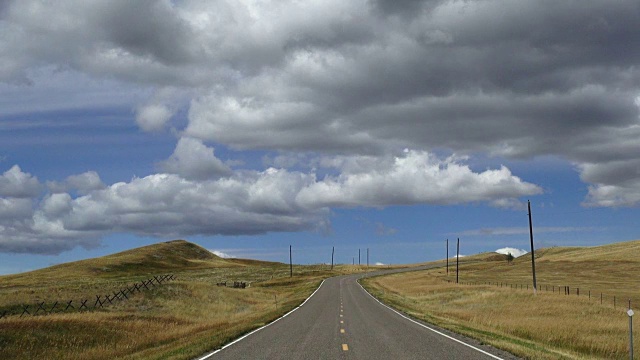 宽阔的视角，空铺的道路与蓬松的云和蓝天与阴影滚动横跨景观。视频素材