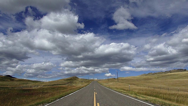 宽阔的视角，空铺的道路与蓬松的云和蓝天与阴影滚动横跨景观。视频素材