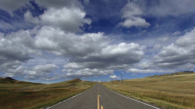 宽阔的视角，空铺的道路与蓬松的云和蓝天与阴影滚动横跨景观。视频素材