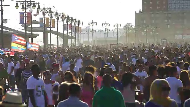 镜头捕捉到了走在科尼岛木板路上的人群。一艘大型游轮在海面上行驶，后面跟着人群。视频素材