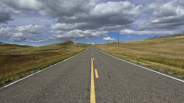 低广角视野的空铺砌道路与蓬松的云和蓝天与阴影滚动横跨景观。视频素材