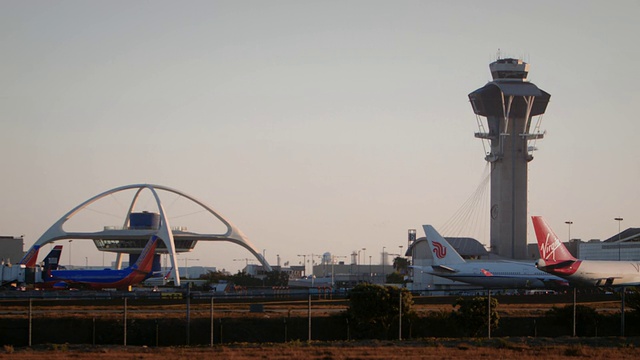 在洛杉矶国际机场控制塔和主题餐厅附近，维珍美国空中客车A319横过机身降落，背景是第二架飞机起飞视频素材