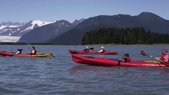 四只海上皮划艇在大海中划着，身后是群山和冰川视频下载