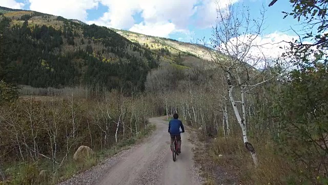 一个年轻的白人男子正在一条绿树成荫的山路上骑自行车视频素材