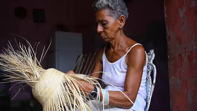 古巴妇女在贫困的房子里制作一顶草帽，在纪念品摊上卖给游客视频素材