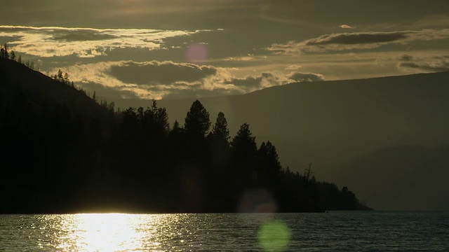 夕阳映照在水面上，将山树置于背光中视频素材