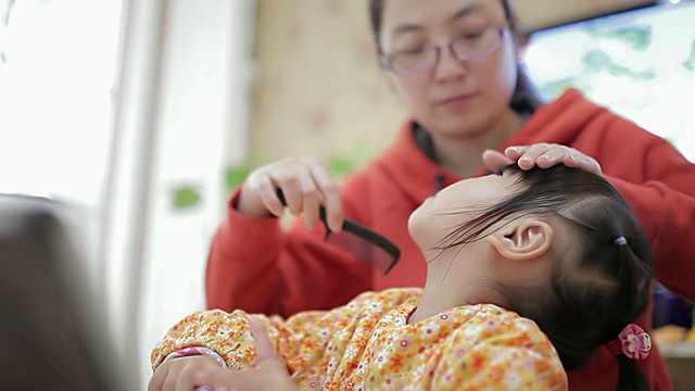 母亲给女儿梳头，女儿用手机看电影的CU镜头/陕西西安，中国视频素材