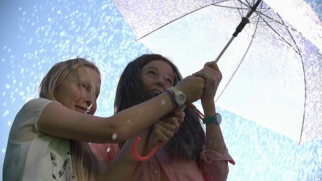 两名少女在雨伞下笑着躲避夏天的雨点阵雨/新西兰奥克兰视频素材