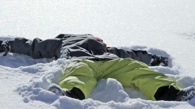 一个小男孩在一个阳光明媚的冬日里做了一个雪天使视频素材