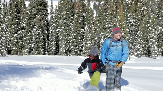 在一个阳光明媚的冬日里，爸爸和儿子走在雪地上视频素材