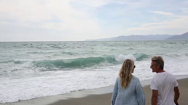 一对夫妇沿着海滩走向汹涌的海浪视频素材