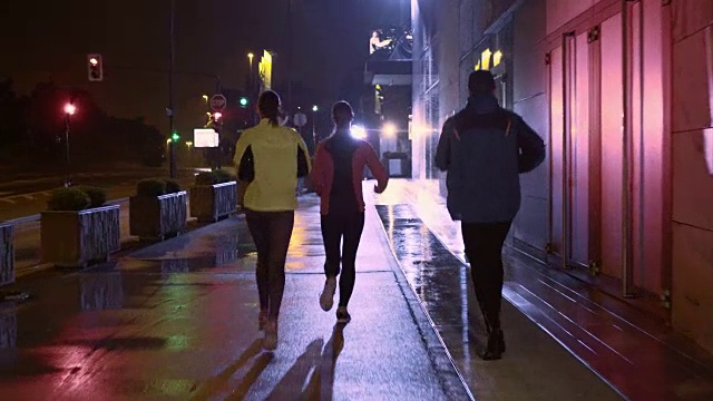 朋友们在一个雨夜在城市里跑步视频素材