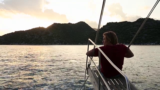 在风平浪静的海湾里，年轻人在帆船的吊杆上休息视频素材