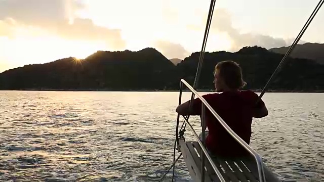 在风平浪静的海湾里，年轻人在帆船的吊杆上休息视频素材