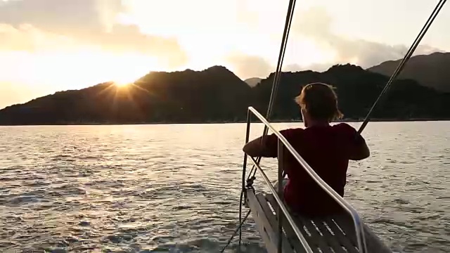 在风平浪静的海湾里，年轻人在帆船的吊杆上休息视频素材