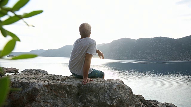 一个成熟的男人从岩石向宁静的海湾眺望视频素材