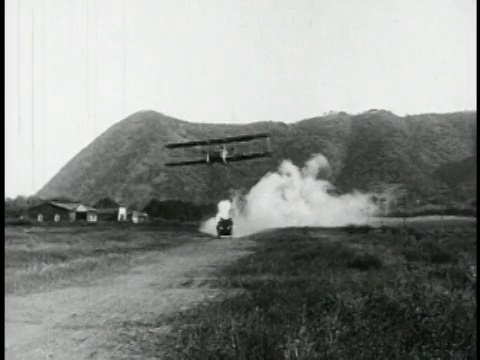 一架1910年代的双翼飞机飞过在土路上行驶的警车+对飞机射击/特征视频素材