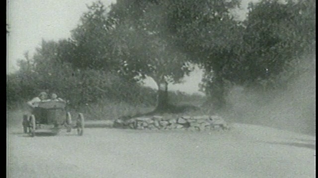 1915年，一名男子和一名女子在乡村道路上驾车绕着路中心的树行驶视频素材