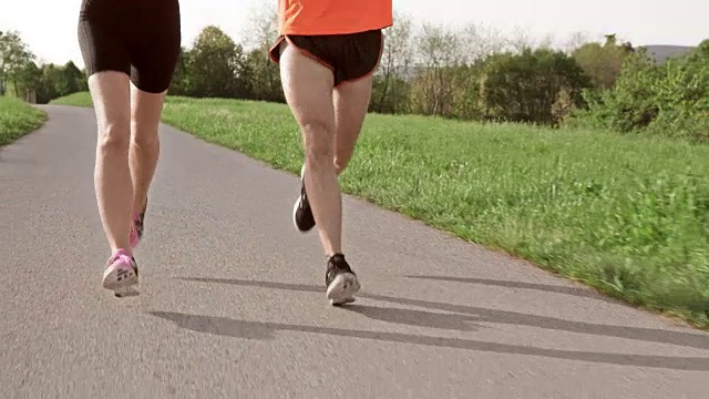 SLO MO TS一对在沥青上跑步的夫妇的腿视频素材