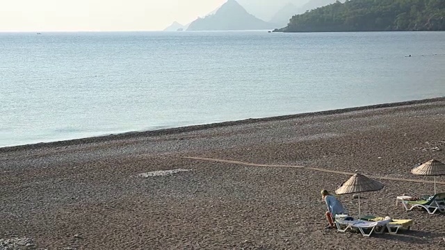 远处的女人走过空荡荡的海滩，群山视频素材