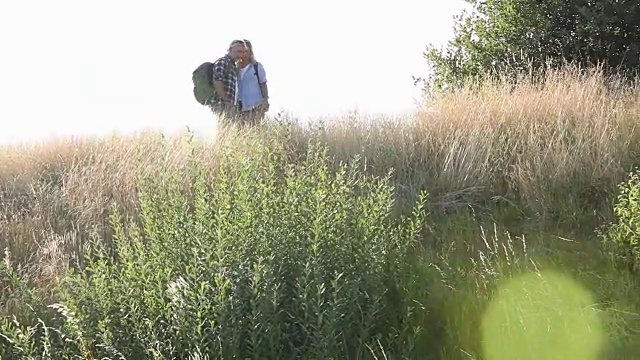 一对成年夫妇背着背包在草丛中徒步旅行视频下载