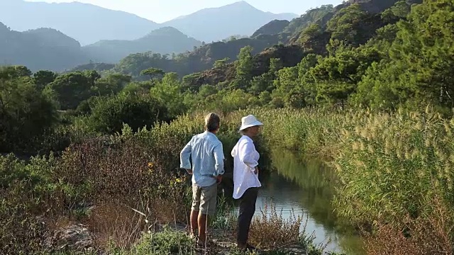 一对情侣沿着池塘边散步，望向群山视频素材