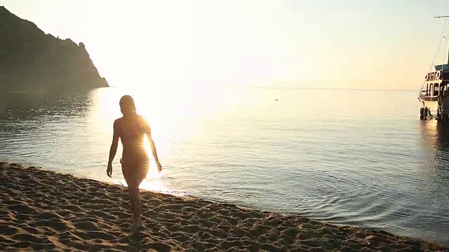 年轻女子离开大海，在日出时走上海滩视频素材