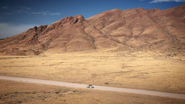 WS AERIAL TU T/L View of High bare mountain behind sparse landscape with road and tiny all terrain vehicle, Naukluft, Windhoek，纳米比亚视频素材