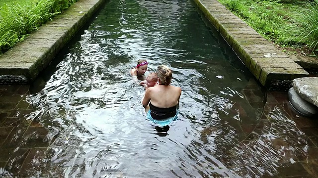 印尼巴厘岛乌布，一名年轻女孩在游泳池游泳时，母亲抱着她的孩子视频素材