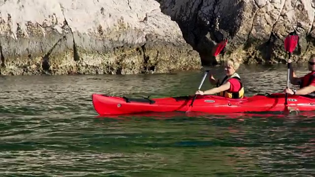 一对夫妇沿着岩石海岸划皮艇视频素材