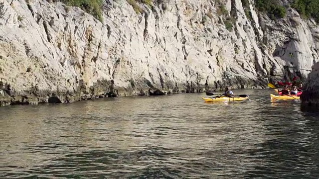 朋友们沿着岩石海岸划皮艇视频素材