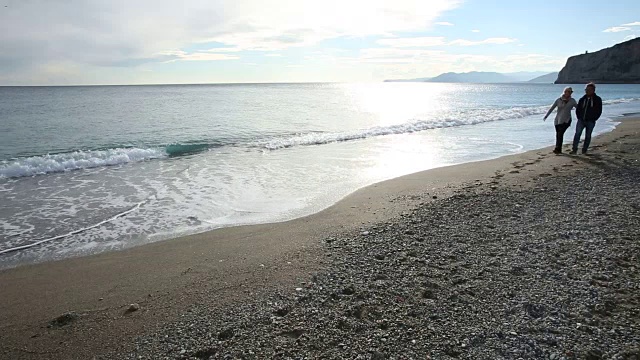 一对夫妇沿着海滩散步，靠近冲浪边缘视频素材