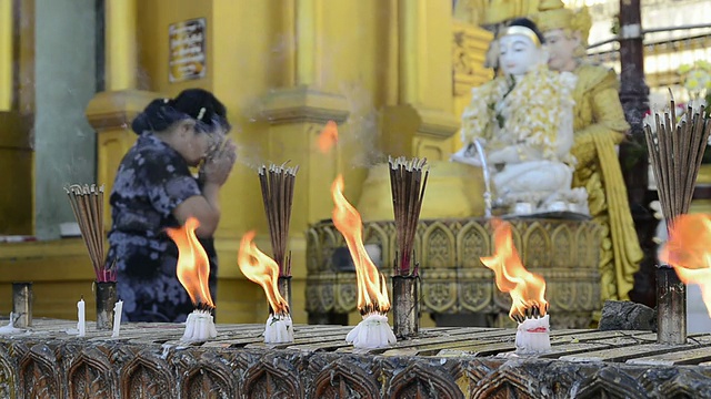 缅甸仰光大金塔中，一名女子在佛像前祈祷，蜡烛和香火燃烧视频素材